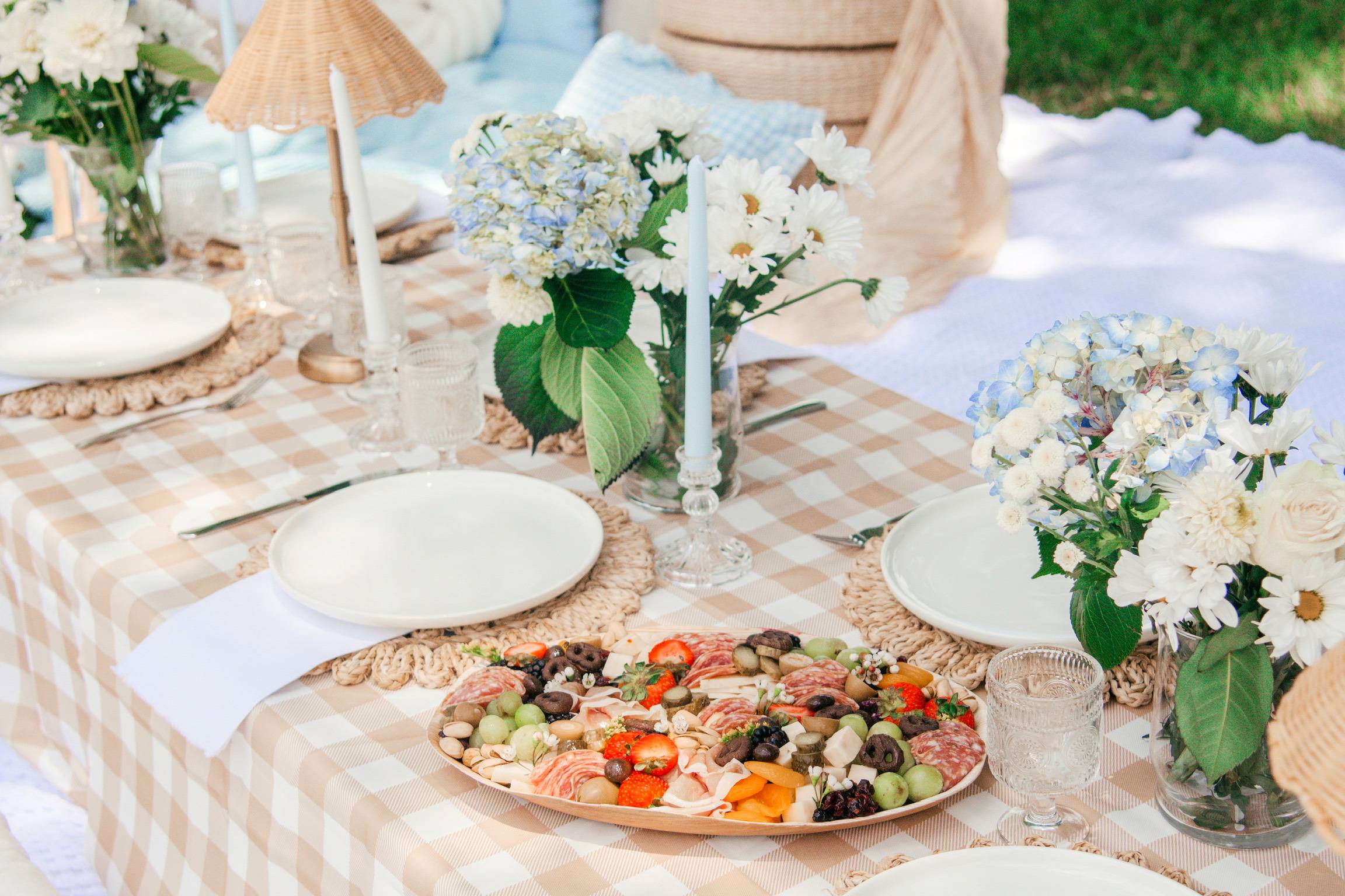 Charcuterie, blue hydrangeas and candles on a gingham picnic table